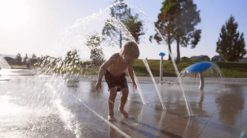 3 year old boy walks under water arches at splash pad in slow motion Stock Footage 233942749