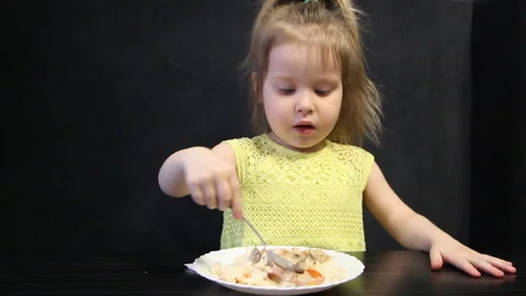 3 year old child eats cooked rice and mushrooms with a spoon on a black Stock Footage 111332531