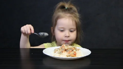 3 year old child eats cooked rice and mushrooms with a spoon on a black Stock Footage 111333275
