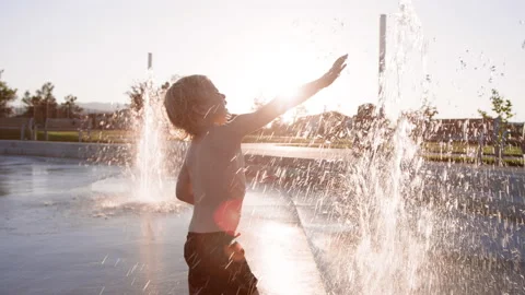 3 year old reaches to touch tall water spray at splash pad against summer sunset Vídeo Stock 233947779