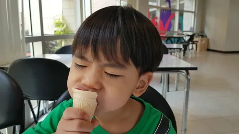 A 3 years old Asian boy enjoys a delicious ice cream cone. Little kid is eating Stock Footage 150473061