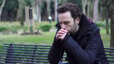 30 year old Caucasian worried man sitting alone in the park Stock Footage