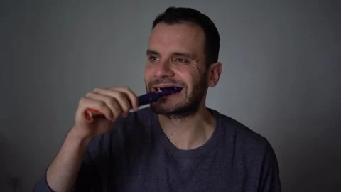 30-year-old man brushes his teeth with purple toothpaste using an electric .. Stock Footage 294524190