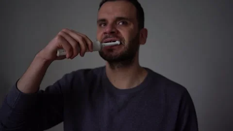 30-year-old man brushes his teeth with purple toothpaste using an electric .. Stock Footage 294524250