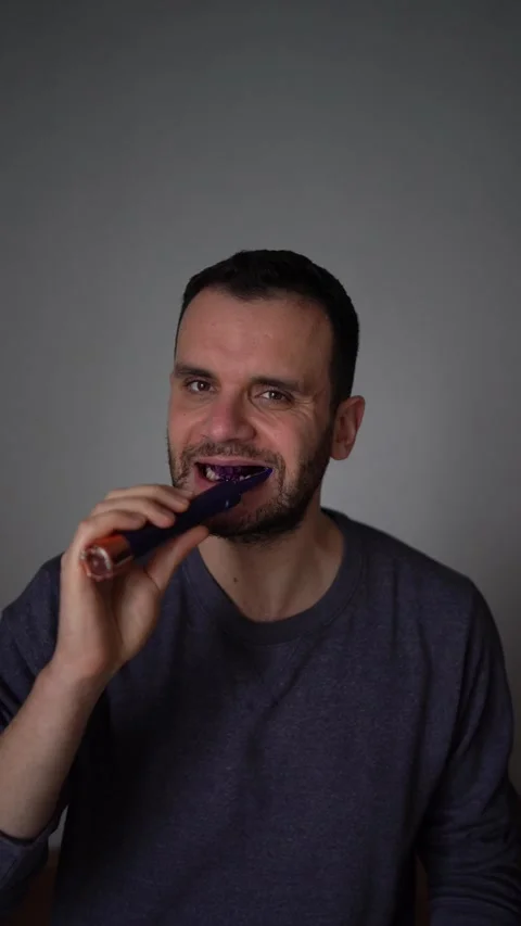 30-year-old man brushes his teeth with purple toothpaste using an electric .. Stock Footage 294524873