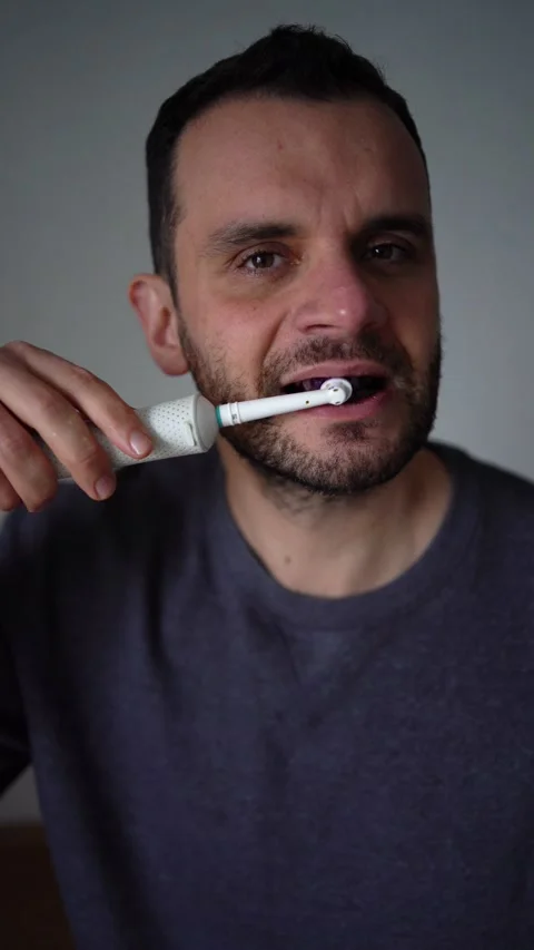 30-year-old man brushes his teeth with purple toothpaste using an electric .. Stock Footage 294525078