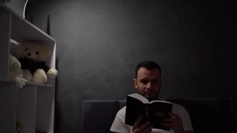 30 year old man reading bible and praying in bed with lamp light, evening r.. Stock Footage 294521590