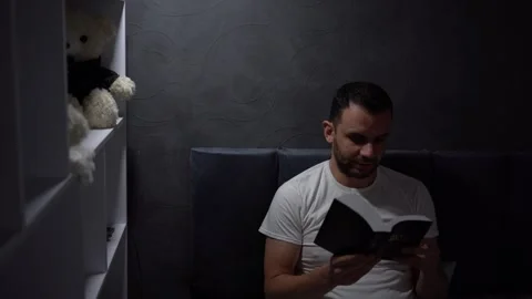 30 year old man reading bible and praying in bed with lamp light, evening r.. Stock Footage 294525080
