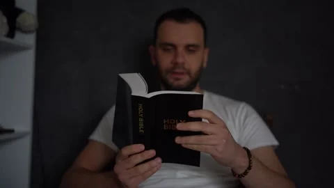 A 30-year-old man reads the Bible and prays in bed, morning routine Stock Footage 294522096