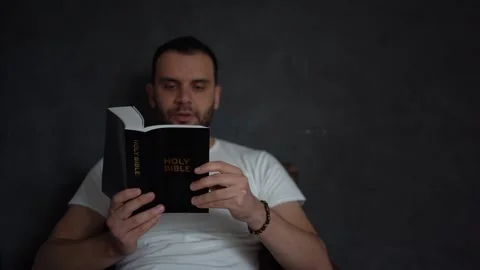 A 30-year-old man reads the Bible and prays in bed, morning routine Stock Footage 294522966