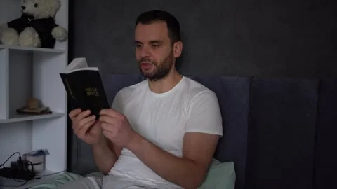 A 30-year-old man reads the Bible and prays in bed, morning routine Stock Footage 294524290
