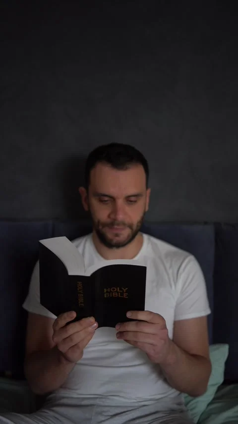 A 30-year-old man reads the Bible and prays in bed, morning routine Stock Footage 294524343