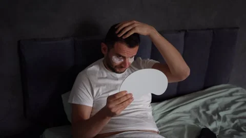 30-year-old man with a silk mask for sleep applying patches under the eyes .. Stock Footage 294522095