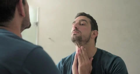 30s man touching lip, leaning into bathroom mirror, checking stubble and Stock Footage 340982014