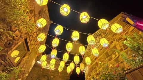 31  glowing yellow lanterns hanging above ancient stone alley at night Stock Footage 345884883