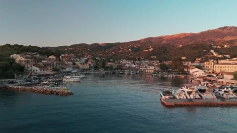 Drone Approach Over Kassiopi Harbor and Rooftops Towards Mountains at Sunrise Drone Approach Over Kassiopi Harbor and Rooftops Towards Mountains at Sunrise
