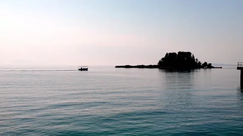 Sunset View of Pontikonisi Island and Small Boat Moving Over Calm Ionian Sea Sunset View of Pontikonisi Island and Small Boat Moving Over Calm Ionian Sea
