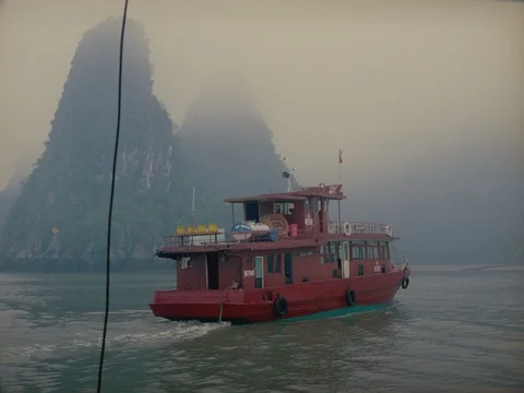 35MM 2K EXT DAY-HA LONG BAY VIETNAM- CAM MOVING W RED BOAT W LIMESTONE TOWERS Stock Footage 75373487