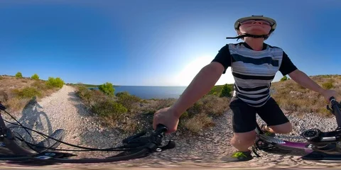 360VR video of female mountain biker riding on gravel road along the coastline Stock Footage 95040407