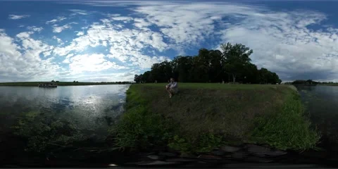 360Vr Video Man is Sitting on a River Bank Green Grass Leisure Boat is Floating Stock Footage 65169926