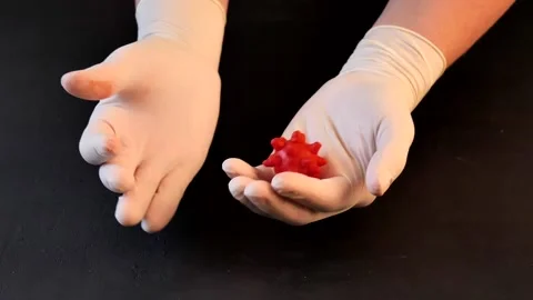 3D model of red coronavirus lies in hands in white medical disposable latex Stock Footage 152565646