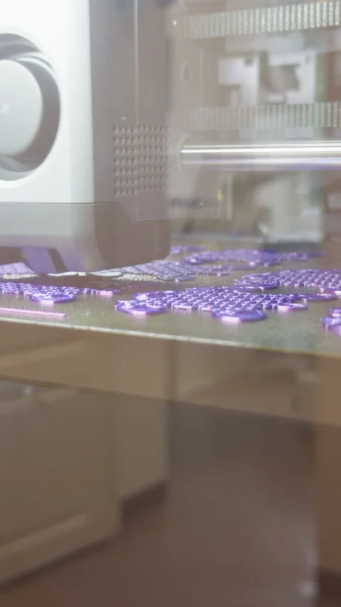 3D printer creating purple puzzle pieces on build plate in bright workshop light Stock-Footage 346558778