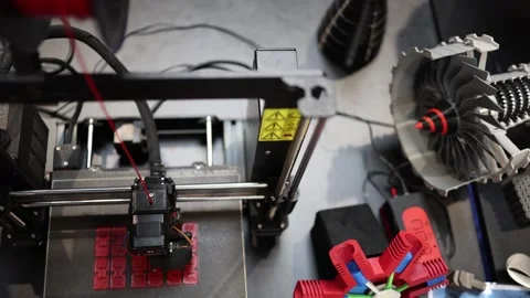 3D printer extruding red filament while colorful turbine prototype and jet engin Stock Footage 311047087