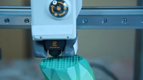 3D printer nozzle extruding plastic filament to create a green object. Stockbeeldmateriaal 336198977