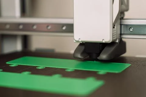3D printer nozzle printing green plastic components on dark build plate Foto stock