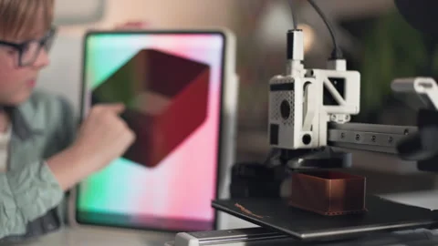 3D printer in operation in the foreground with kid on background with tablet Stock Footage 335380000