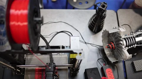 3D printer working with red filament creating prototype parts next to detailed j Stock Footage 311047270