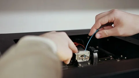 3D technology two men's hands push plastic gray thread into prongs of printer Stock Footage 124375394