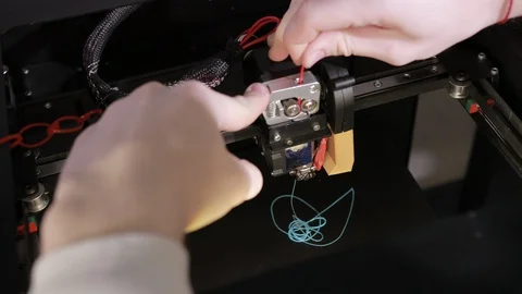 3D technology two men's hands push plastic gray thread into prongs of printer Stock Footage 124716230