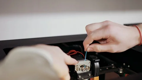 3D technology two men's hands push plastic gray thread into prongs of printer Stock Footage 124716636
