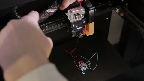 3D technology two men's hands push plastic gray thread into prongs of printer Stock Footage 125130158