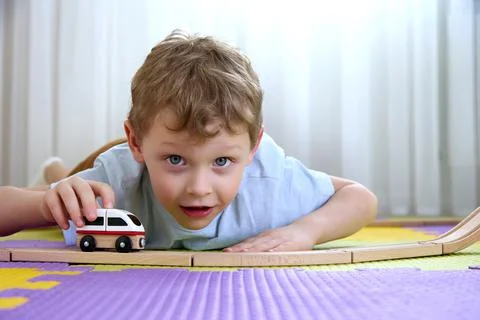 4-5 year old boy looks into camera and plays with a train and a wooden railway Stock Photos