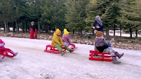 4 children on red sleighs going down a small hill surrounded by turkish moms Stock Footage 231128400