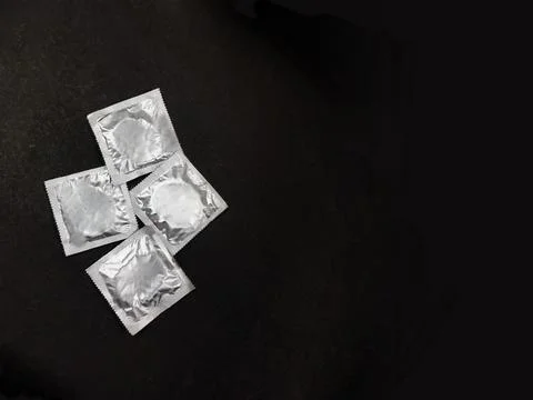 4 condom packets placed on black background top view with copy space. Stock Photos