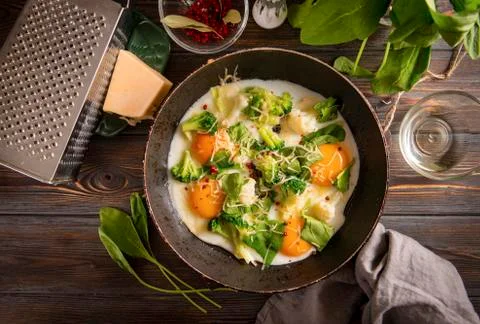 4 fried eggs with broccoli, spinach, spices and cheese in a pan on a dark woo Stock Photos
