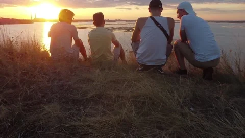 4 friends sit on the edge of a cliff and watch the sunset. The guy shoots a Stock Footage 137178480