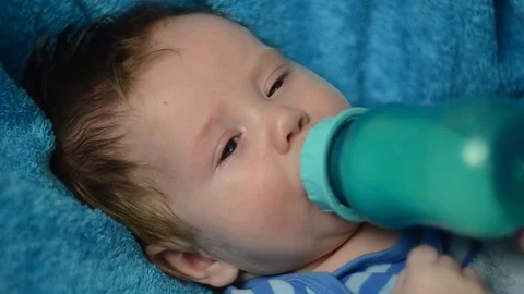 A 4 month old boy drinks milk from a bottle and looks at the camera. close up Stock Footage 114968185