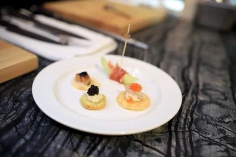 4 small canapes are placed on a white round plate. The table surface is a mar Stock Photos