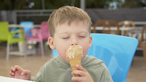 4-year-old boy enjoys eating white ice cream from cone, happily licking and Stock Footage 315670252