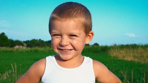 4-year-old boy in a white t-shirt shyly smiles into the camera, then looks away Stock Footage 94233136