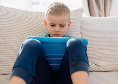 4-yearold boy sits on a sofa at home with a tablet Foto stock