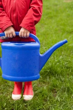 4 years old boy in a red jacket and rubber boots is going to water a tree and Stock Photos