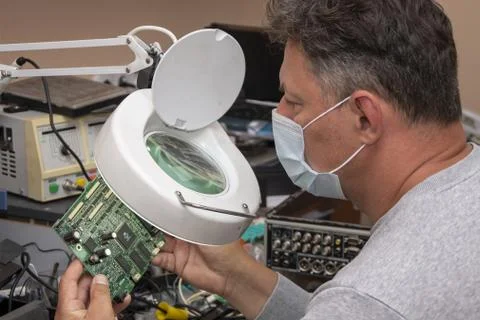 A 40-45-year-old man in a medical mask looks through a magnifying lens Stock Photos