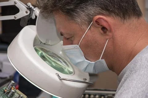 A 40-45-year-old man in a medical mask looks through a magnifying glass Stock-Fotos
