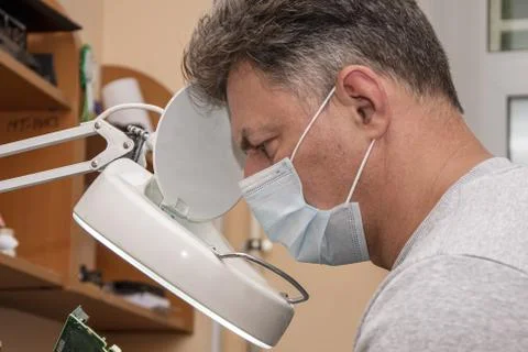 A 40-45-year-old man in a medical mask looks through a magnifying glass at an 写真素材