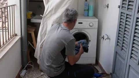 A 40-year-old man with gray hair loading clothes in the washing machine Stock Footage 140750857